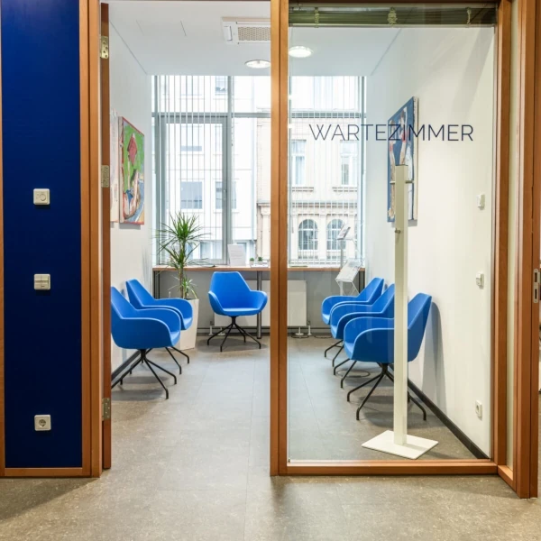 Modernes Wartezimmer mit blauen Stühlen, großen Fenstern und heller Raumgestaltung.