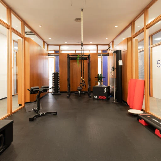 Modernes Fitnessstudio mit Trainingsgeräten, Hanteln und Fitnessmatten in hellem Raum.