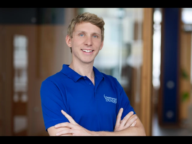 Junger Mann im blauen Polohemd steht lächelnd im modernen Büro und verschränkt die Arme.